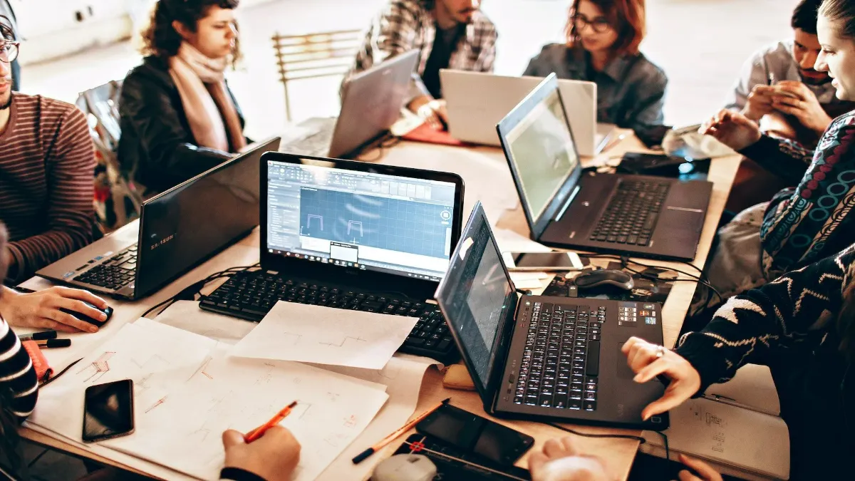 Overzichtsfoto van een team dat rond een tafel samenwerkt op meerdere laptops, tussen schetsen en notities door